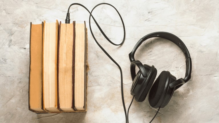 Books and headphones connected to them on a white stone background. Concept Audiobooks.